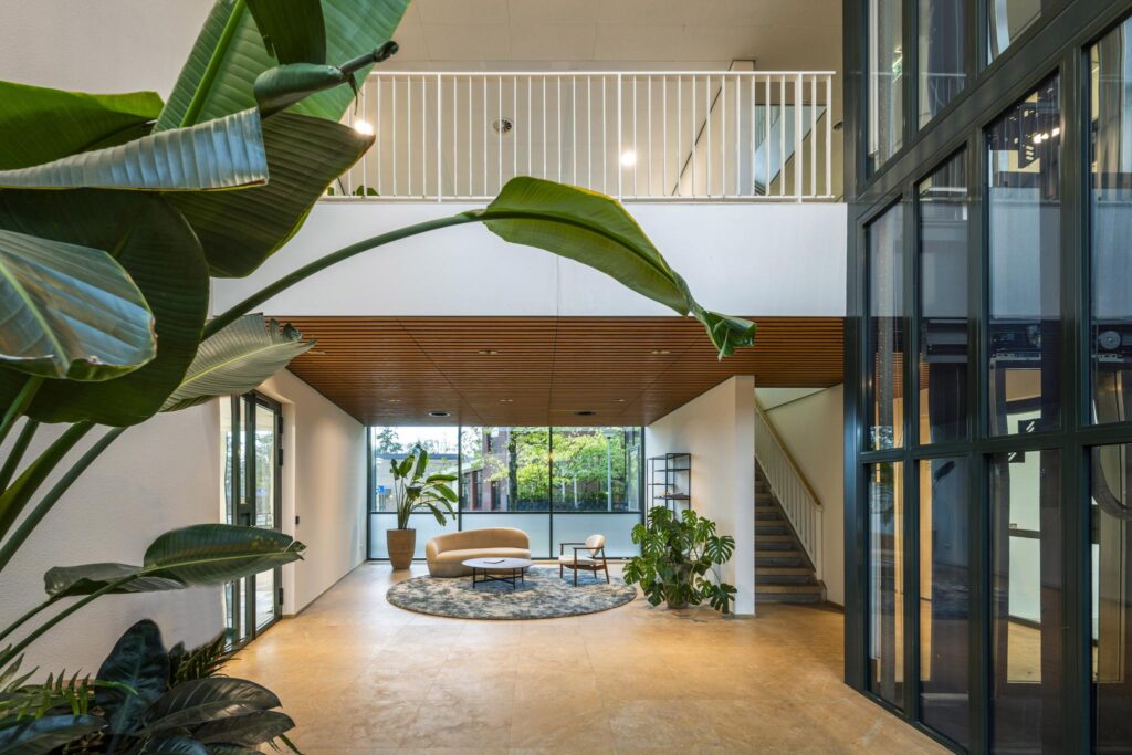 Moderne, lichte ontvangsthal aan de De Cuserstraat met zithoek, grote planten en glazen lift.